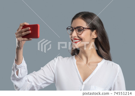 Woman with glasses holding smartphone at face level 74551214