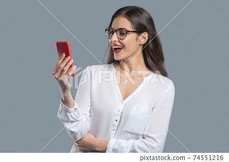 Enthusiastic woman looking at smartphone in outstretched hand Enthusiastic woman looking at smartphone in outstretched hand 74551216