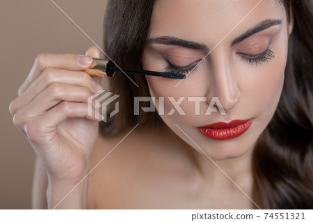 Woman in process of applying mascara on eyelashes Woman in process of applying mascara on eyelashes 74551321
