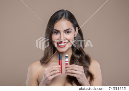Happy beautiful woman presenting red lip glosses Happy beautiful woman presenting red lip glosses 74551335