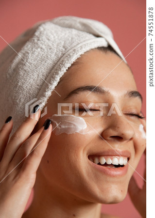 Girl applying moisturizing cream on her face 74551878