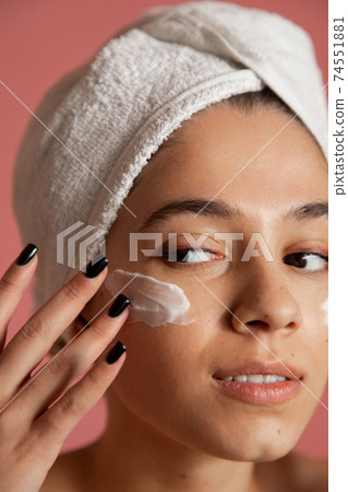 Woman applying the moisturizer cream on her face 74551881