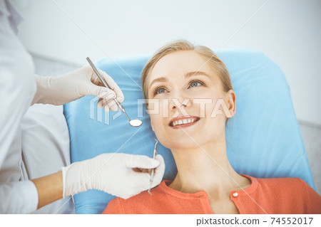 Happy smiling woman is being examined by dentist at dental clinic. Healthy teeth and medicine, stomatology concept 74552017