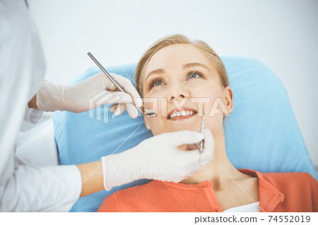 Happy smiling woman is being examined by dentist at dental clinic. Healthy teeth and medicine, stomatology concept Happy smiling woman is being examined by dentist at dental clinic. Healthy teeth and medicine, stomatology concept 74552019
