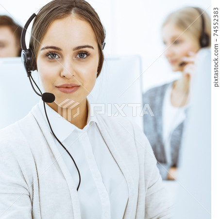Call center. Group of diverse operators at work. Beautiful woman in headset communicating with customers of telemarketing service. Business concept 74552383