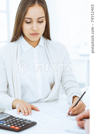 Young business woman and man sitting and working with computer and calculator in office. Bookkeeper checking balance or making finance report. Tax and audit concepts Young business woman and man sitting and working with computer and calculator in office. Bookkeeper checking balance or making finance report. Tax and audit concepts 74552403