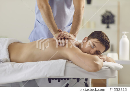 Young man with eyes closed enjoying procedure of medical massage from professional masseur 74552813