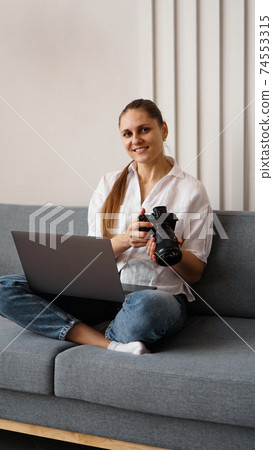 Happy young woman with photo camera using laptop at home 74553315