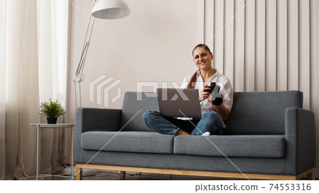 Happy young woman with photo camera using laptop at home 74553316