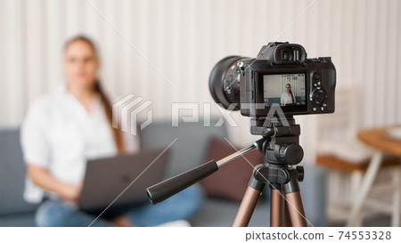 Blogger recording video indoors, selective focus on camera display 74553328