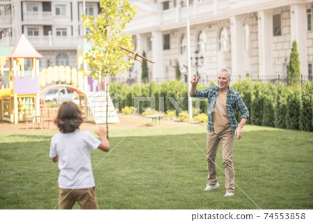 Dad and son playing together on a lawn and looking involved Dad and son playing together on a lawn and looking involved 74553858