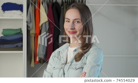 Portrait of a woman who stands against the background of a large wardrobe a wardrobe with stylish clothes and household items Portrait of a woman who stands against the background of a large wardrobe a wardrobe with stylish clothes and household items 74554029