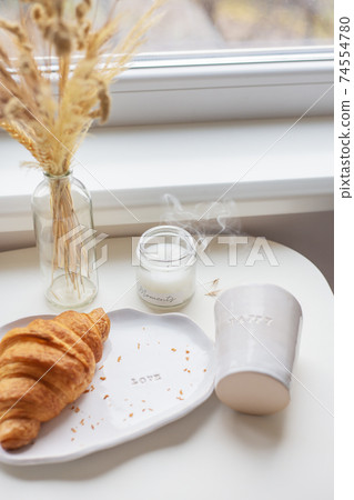 White glass and a plate on which lies a croissant made of clay with the inscription love, handmade. White glass and a plate on which lies a croissant made of clay with the inscription love, handmade. 74554780