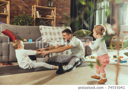 Young man exercising fitness, aerobic, yoga at home, sporty lifestyle. Getting active while his child playing on the background, home gym. Young man exercising fitness, aerobic, yoga at home, sporty lifestyle. Getting active while his child playing on the background, home gym. 74555041