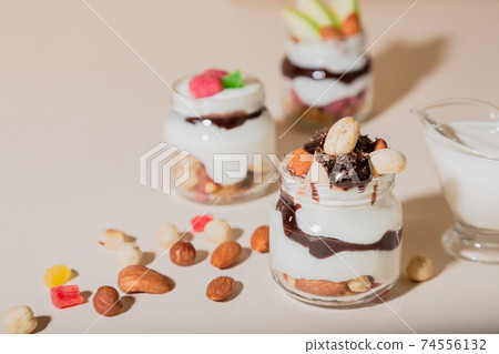 Sweet tasty milk curd creamy food in a glass jar of homemade breakfast. Cheesecake, English Trifle, Eton dessert, tiramisu, zuppa Inglese with nuts, almonds, cashews, hazelnuts, candied fruits and Sweet tasty milk curd creamy food in a glass jar of homemade breakfast. Cheesecake, English Trifle, Eton dessert, tiramisu, zuppa Inglese with nuts, almonds, cashews, hazelnuts, candied fruits and 74556132