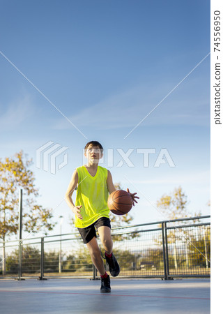 Cute boy in yellow shirt plays basketball on city playground. Cute boy in yellow shirt plays basketball on city playground. 74556950