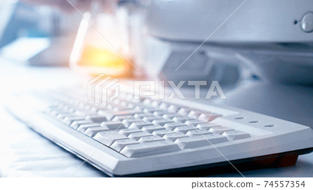 Computer keyboard and test tube with orange liquid in the laboratory. The concept of conducting experiments in chemistry and medicine, copy space 74557354