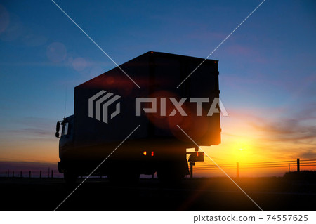 Truck driver transports cargo on a truck against the backdrop of sunset at night. The concept of compliance with the work and rest regime of drivers Truck driver transports cargo on a truck against the backdrop of sunset at night. The concept of compliance with the work and rest regime of drivers 74557625