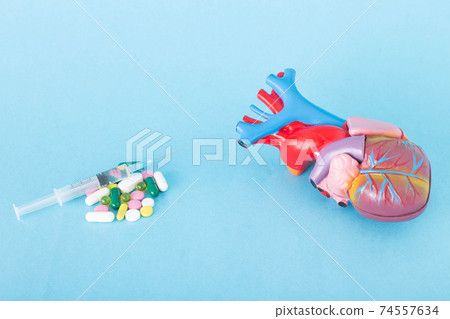 Mock up human heart on a blue background and a handful of pills with a syringe. Cardiovascular system treatment concept and anti-atherosclerosis therapy Mock up human heart on a blue background and a handful of pills with a syringe. Cardiovascular system treatment concept and anti-atherosclerosis therapy 74557634