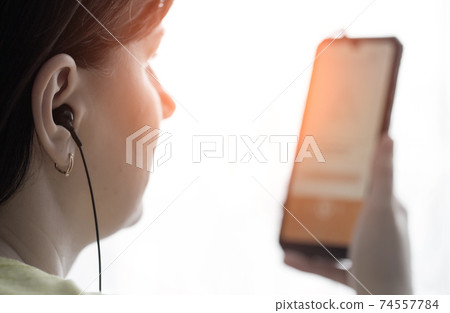 A girl with headphones in her ears holds a smartphone on the background of the sunset. The concept of listening to music in modern stereo headphones A girl with headphones in her ears holds a smartphone on the background of the sunset. The concept of listening to music in modern stereo headphones 74557784