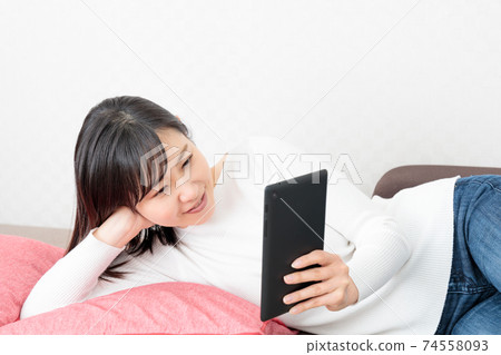 Woman lying on the couch and holding a tablet Woman lying on the couch and holding a tablet 74558093