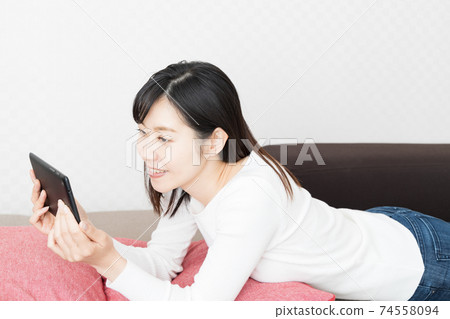 Woman lying on the couch and holding a tablet Woman lying on the couch and holding a tablet 74558094