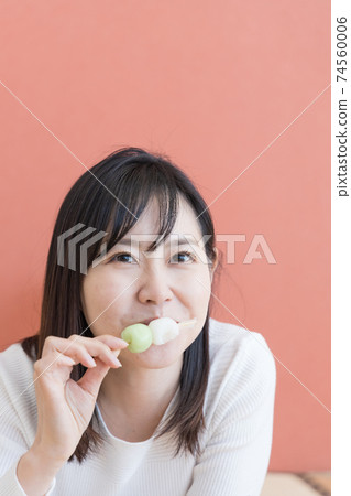 A woman lying down in a Japanese-style room and eating dumplings 74560006