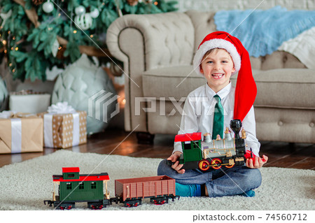 Good morning. Happy little boy with a gift, toy train, under the Christmas tree on New Year's morning. Time to fulfill wishes. 74560712