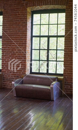 Brownish brick wall with leather sofa. Background photo with copy space for text. Claret leather sofa to the loft an interior with a bright searchlight and a window. brick wall. Leather sofa in a 74561044