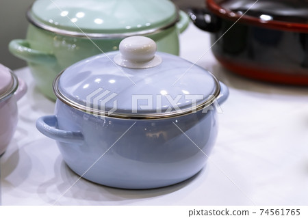 Many enameled steel metal multicolored new modern cooking pots enamelware stand on a shelf in the kitchen. Household goods, dishes, kitchen utensils. Shop window, sale of domestic products, interior 74561765