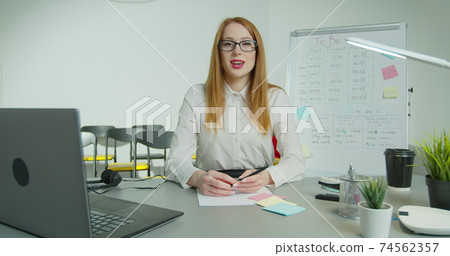 English teacher virtual teaching look at webcam give distance lesson. Female school tutor explain online class talking to camera sit at desk in classroom. Video conference call education. English teacher virtual teaching look at webcam give distance lesson. Female school tutor explain online class talking to camera sit at desk in classroom. Video conference call education. 74562357