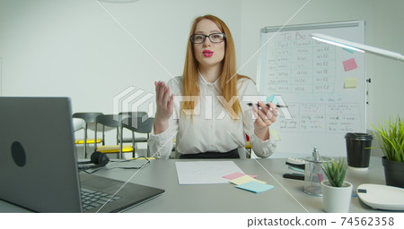 English teacher virtual teaching look at webcam give distance lesson. Female school tutor explain online class talking to camera sit at desk in classroom. Video conference call education. English teacher virtual teaching look at webcam give distance lesson. Female school tutor explain online class talking to camera sit at desk in classroom. Video conference call education. 74562358
