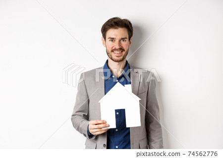 Real estate. Handsome young businessman buying property, holding paper house cutout and smiling, agency advertisement, white background 74562776