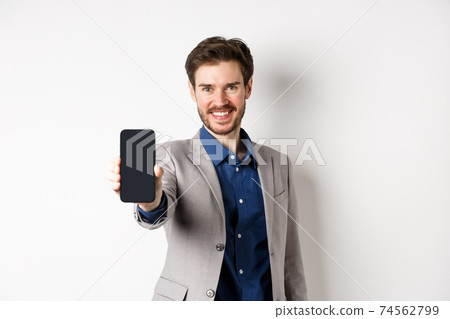 E-commerce and online shopping concept. Confident businessman in suit stretch out hand with empty smartphone screen, showing on phone, standing against white background 74562799