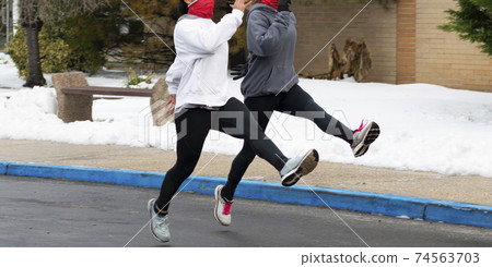 Two girls running track speed drills in a parking lot because of snow 74563703