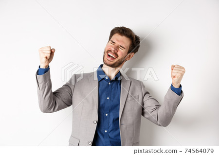 Successful business man in suit winning prize, shouting yes with relieved smile and fist pumps, celebrating achievement and success, standing on white background Successful business man in suit winning prize, shouting yes with relieved smile and fist pumps, celebrating achievement and success, standing on white background 74564079