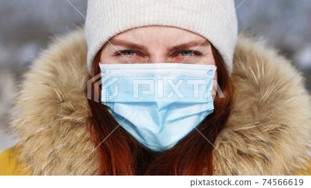 Close up portrait face of young girl in protective medical mask looking at camera in winter time. Safety in public place during coronavirus outbreak. 74566619
