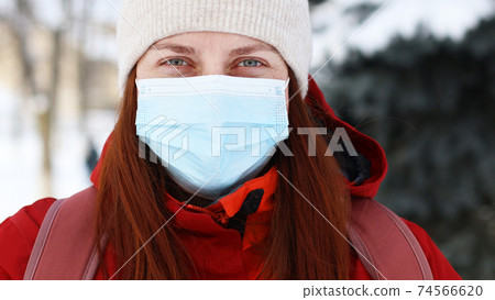 Close up portrait face of young girl in protective medical mask looking at camera in winter time. Safety in public place during coronavirus outbreak. 74566620