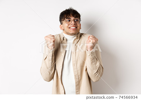 Image of handsome excited man feeling motivated and lucky, looking right and smiling, making fist pump gesture to celebrate victory, winning prize, standing on white background Image of handsome excited man feeling motivated and lucky, looking right and smiling, making fist pump gesture to celebrate victory, winning prize, standing on white background 74566934