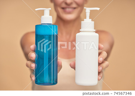 Happy woman holding bottles with natural skincare product in studio Happy woman holding bottles with natural skincare product in studio 74567346