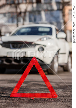 Close up car emergency stop sign on the road. The front fender and right headlight are broken, damaged and scratched on the bumper. 74567529