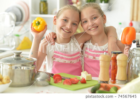 Cute girls preparing delicious fresh salad in kitchen Cute girls preparing delicious fresh salad in kitchen 74567645