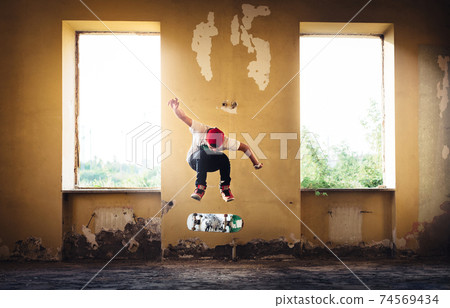 A man captured in middle of skateboarding trick/jump inside an abandoned house directly between two windows, through which sun shines. Focus on man in flight, outer background slightly out of focus. 74569434