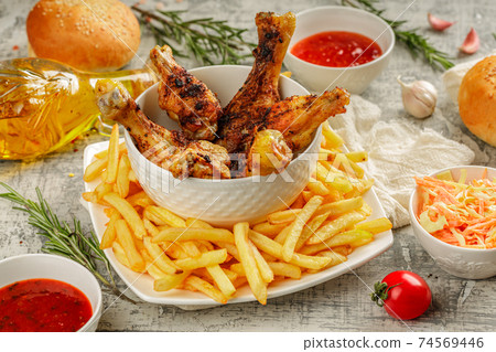 Closeup of a portion of grilled, roasted chicken legs with golden brown crust, served on a white plate with french fries, rosmary, chilly and barbeque sauce 74569446