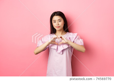 Valentines day concept. Beautiul japanese teen girl show heart gesture and smiling cute, express love and sympathy to lover, standing in romantic dress on pink background 74569770