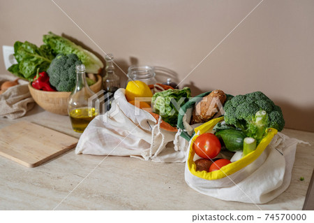 Cotton reusable bags with food products and glass stuff on kitchen table 74570000