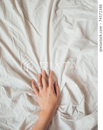 Woman's hand on background of crumpled bed sheet. Creased white linen. Woman touches unmade bed. Cozy imperfect house. Non-ideal cozy home. Woman's hand on background of crumpled bed sheet. Creased white linen. Woman touches unmade bed. Cozy imperfect house. Non-ideal cozy home. 74571386