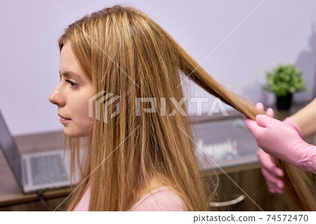 hair diagnostics to young female client by unrecognizable professional cosmetologist 74572470