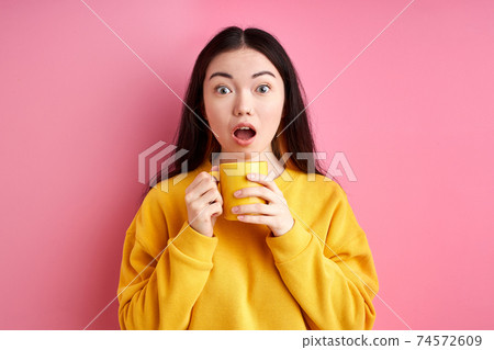 shocked woman with cup in hands, stands with wide opened mouth 74572609