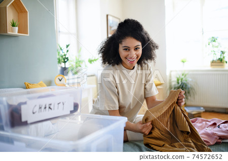 Young woman sorting wardrobe indoors at home, charity donation concept. Young woman sorting wardrobe indoors at home, charity donation concept. 74572652